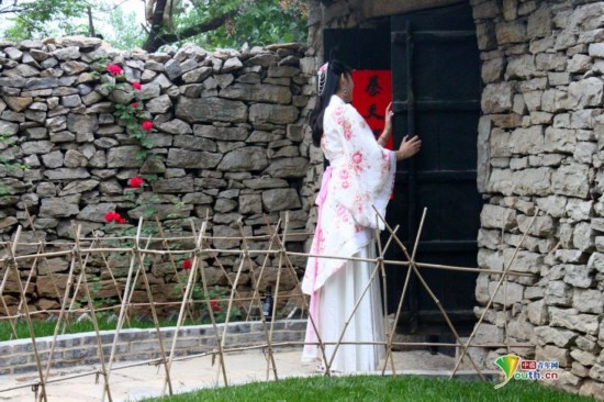 石墙、木门、小花、竹栏与身着汉服的美女背影相映成趣