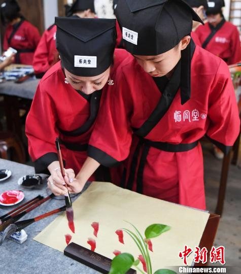 一名身着汉服的中学生家长辅导孩子用毛笔学书画。